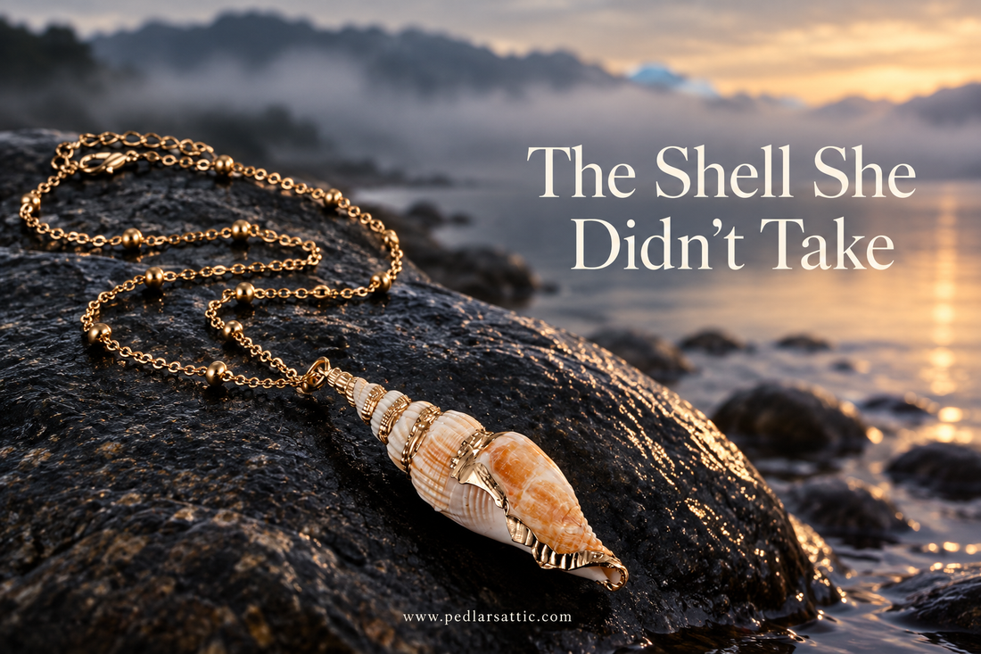 Natural cowrie shell pendant necklace on a dark shoreline stone with misty water behind it.