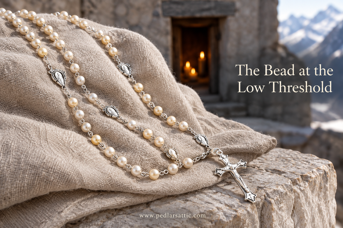 Beige faux-pearl rosary necklace with repeated small Marian medallions and a cross on folded linen and mountain stone.