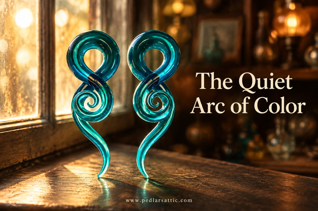 Blue Pyrex glass spiral taper ear gauge pair on a dark surface beside a warm Attic window.